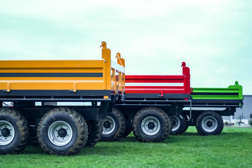 Three colorful farm trailers in a row on grass field.