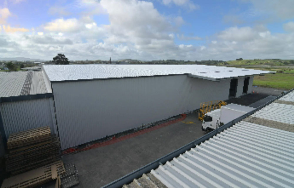Industrial warehouse exterior with corrugated metal roofs and walls, surrounded by pallets and a forklift parked outside.