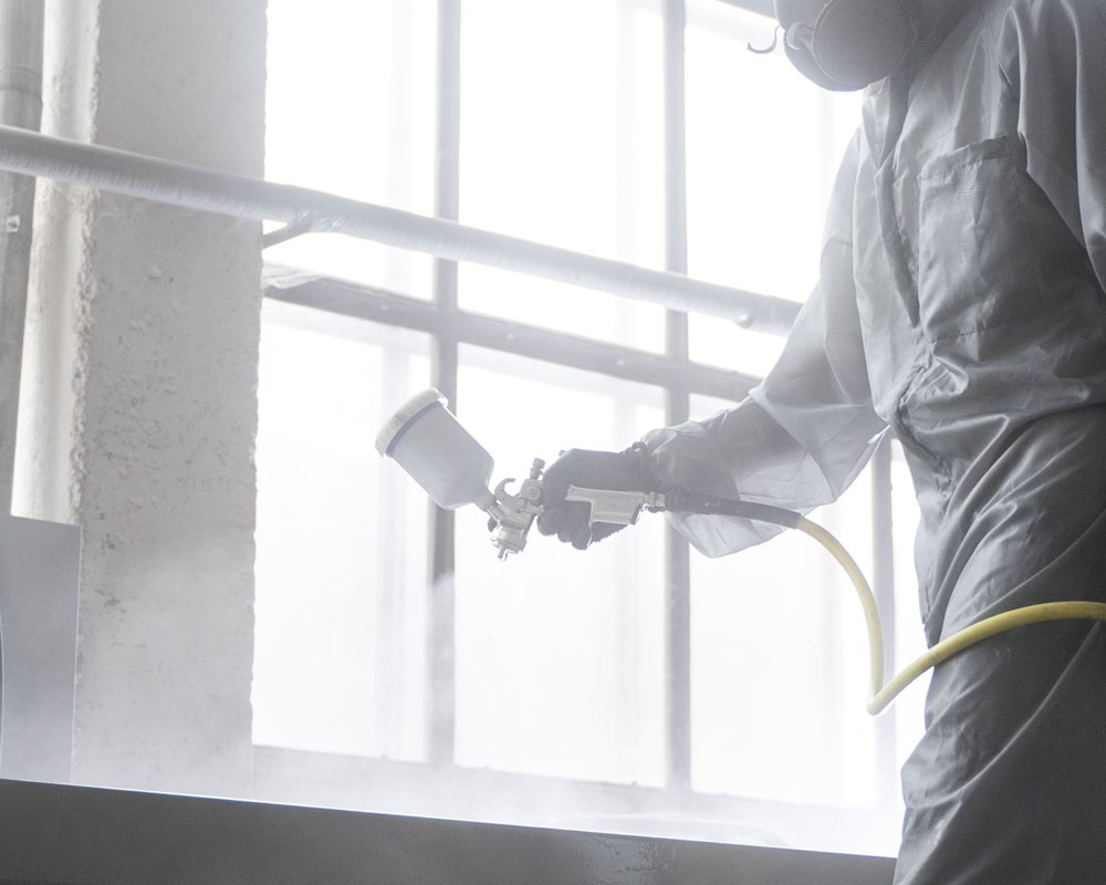Worker in protective gear using a spray gun.